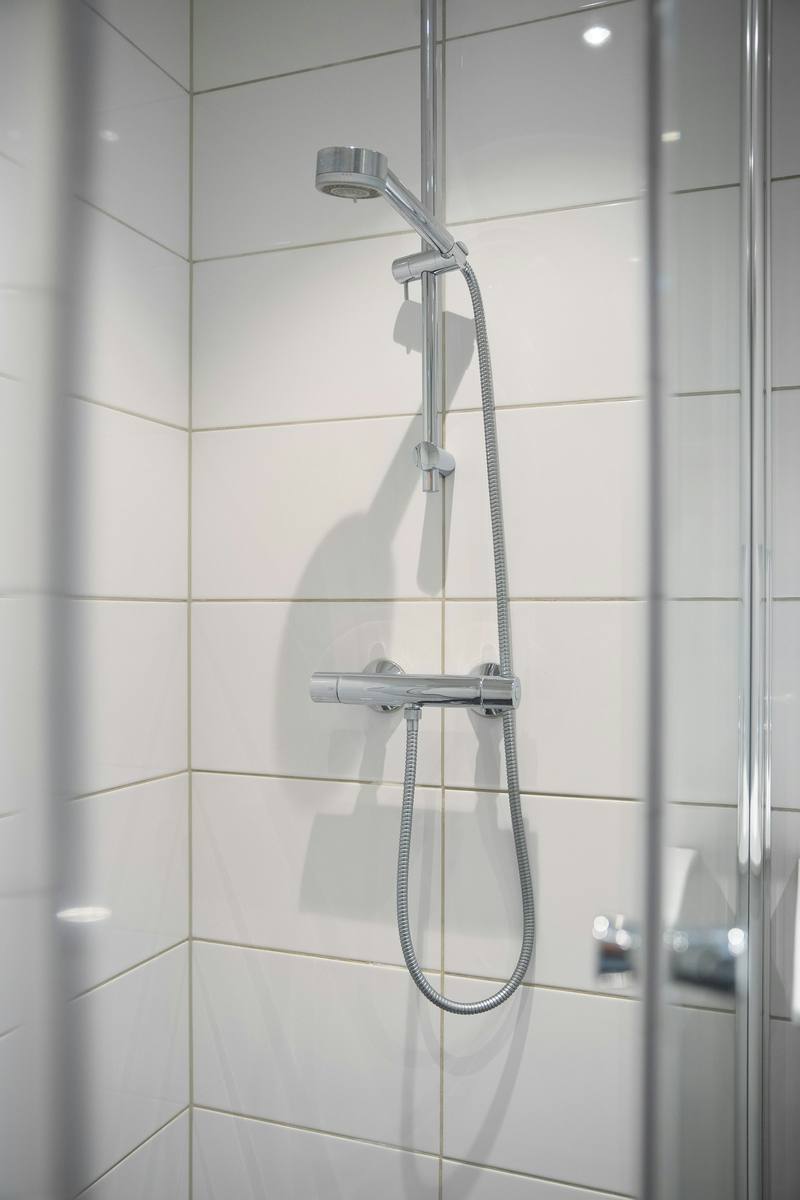 View through the glass panels of a shower door onto white tiles and a chrome hand shower