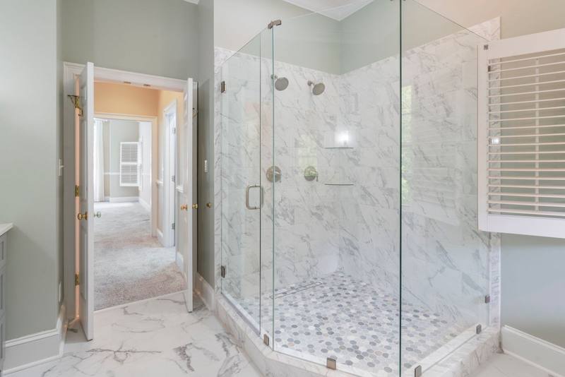 Frameless neo-angle glass shower enclosure on a tiled curb with marble walls