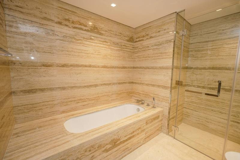 Travertine bathroom with a built-in bathtub next to a glass shower door with chrome handle