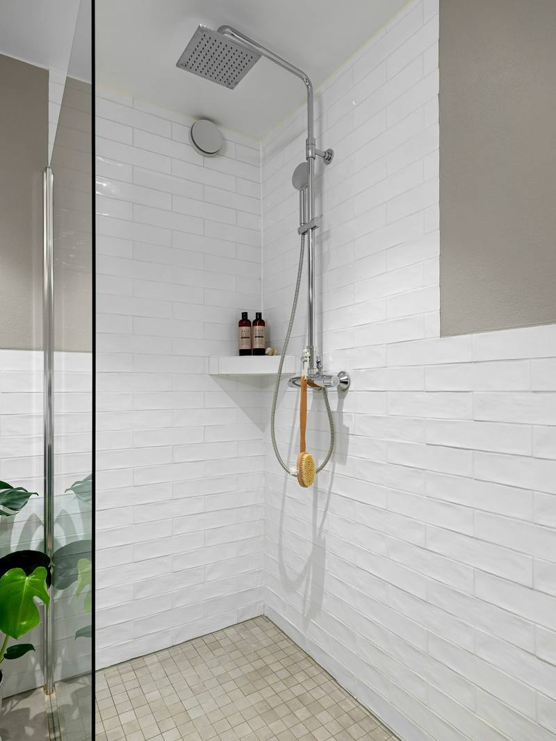White subway-tiled walk-in shower with rain shower column and the edge of a glass door panel