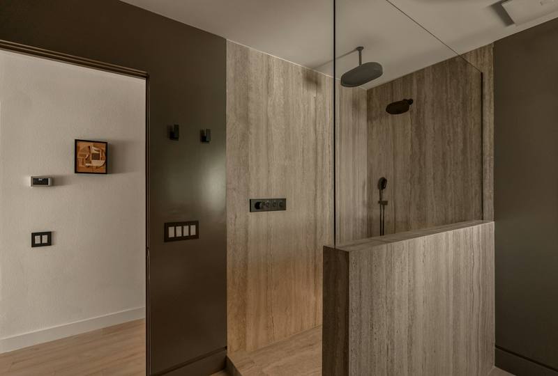 Spa-style walk-in shower with a fixed frameless glass screen and travertine walls