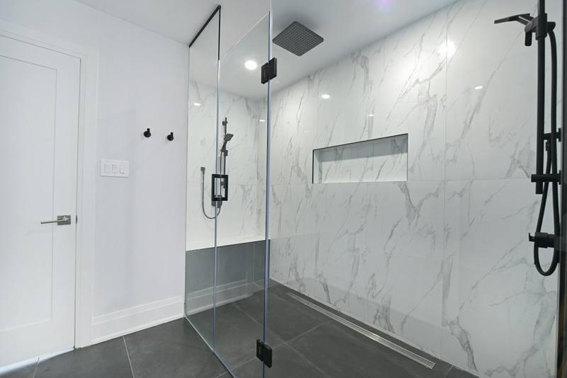 Curbless walk-in shower with frameless glass panels, marble-look tile and a linear floor drain